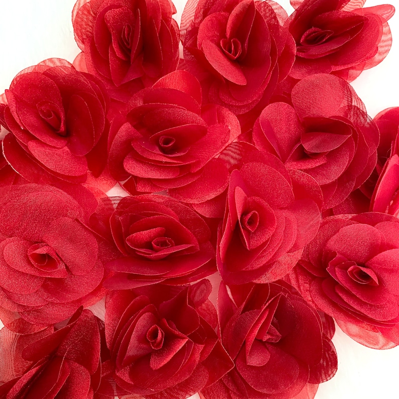 May include: A collection of red fabric rose flower embellishments. The roses are made of a soft, sheer fabric and have a layered, ruffled appearance.