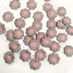 May include: A collection of gray fabric flowers with pink centers. The flowers are arranged on a white lace background.