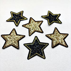 May include: Six star-shaped patches with glittery surfaces. Three stars have gold glitter, and three have dark blue glitter. Each star is outlined with a gold border and a black edge. These patches are suitable for various craft projects.