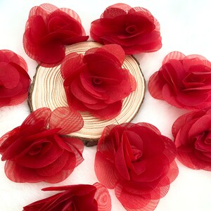 May include: A set of ten red fabric rose flower embellishments. The flowers are made of a soft, sheer fabric and have a delicate, layered look.