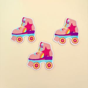 May include: Three pink roller skate patches with rainbow and star details. The patches are embroidered and have a white background.