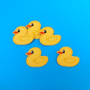 May include: Five yellow rubber ducky patches with orange beaks and eyes. The ducks are arranged in a semi-circle on a blue background.