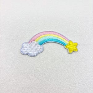May include: Embroidered rainbow patch featuring a pastel rainbow, a white cloud, and a yellow star. The rainbow arcs from left to right, with pink, yellow, and blue stripes. The cloud is on the left, and the star is on the right.