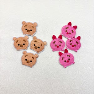 May include: Embroidered patches featuring cartoon bear and pig characters. The bear patches are tan with brown accents, while the pig patches are pink with red accents. These patches are ideal for adding to clothing or accessories.