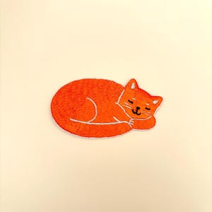 May include: Orange embroidered iron-on patch of a sleeping cat.