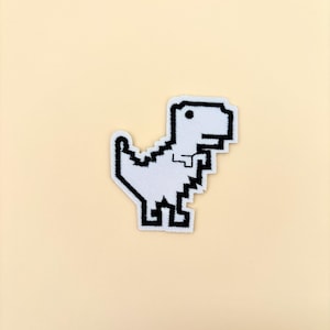 May include: White pixelated dinosaur embroidered patch with black outlines. The dinosaur is facing right and has a small eye.
