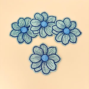 May include: Five blue flower patches with glitter accents. Each flower has a dark blue outline and a lighter blue center. The patches are arranged on a light beige background.