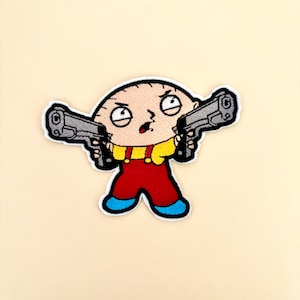 May include: Embroidered patch featuring a cartoon character with a surprised expression, holding two toy guns. The character wears a yellow shirt, red overalls, and blue shoes, with a white border.