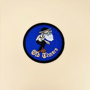 May include: Embroidered patch featuring a cartoon character with a long white beard, wearing a hat and suspenders, on a blue circular background. The words "Old Timers" are in gold lettering around the bottom of the circle. The patch has a black border.