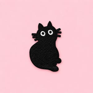 May include: An embroidered patch in the shape of a black cat. The cat has a rounded body, pointed ears, and three whiskers on each side of its face. It features two large, circular white eyes with black pupils, creating a wide-eyed expression.