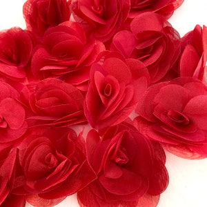 May include: A group of red fabric rose flower embellishments. The flowers are layered and have a ruffled texture.