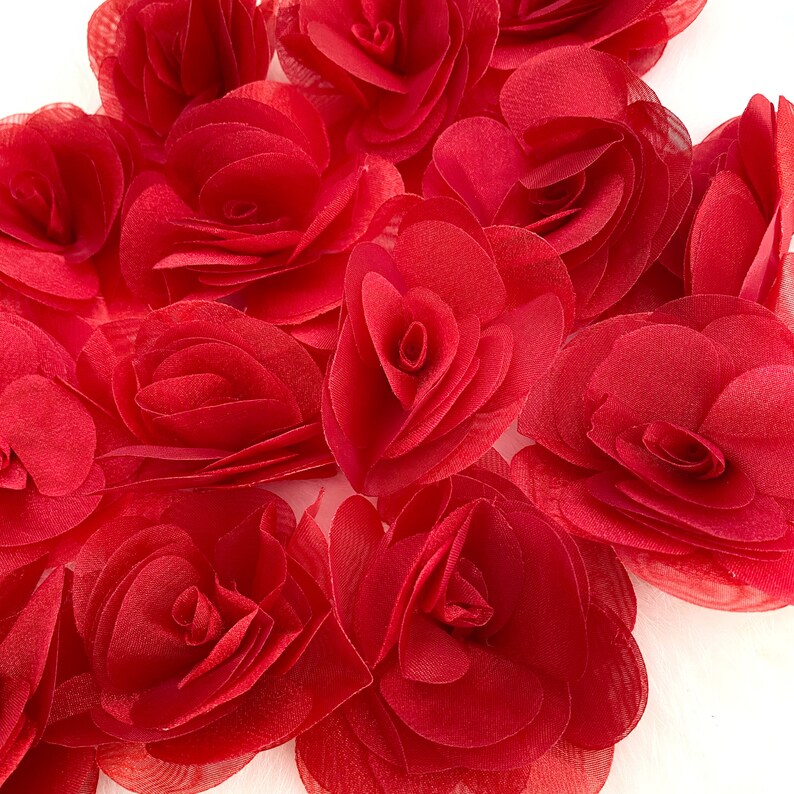 May include: A group of red fabric rose flower embellishments. The flowers are layered and have a ruffled texture.