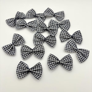 May include: A collection of black and white gingham fabric bows. The bows are arranged on a white surface. The bows are a classic design, suitable for various craft projects or embellishments.