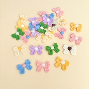 May include: A collection of small, colorful embroidered bows in various shades of yellow, green, pink, blue, purple, and white. Each bow features a contrasting center, creating a charming and decorative effect. These bows are ideal for embellishing crafts or clothing.
