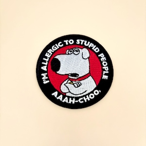May include: Embroidered patch featuring a cartoon dog with the text "I'M ALLERGIC TO STUPID PEOPLE" and "AAAH-CHOO." The patch has a black border, a red background, and a white dog with a red collar.