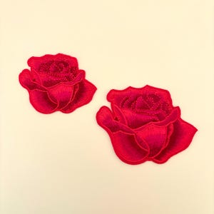 May include: Two bright pink embroidered rose patches. The roses are detailed with stitching and have a slightly 3D effect.
