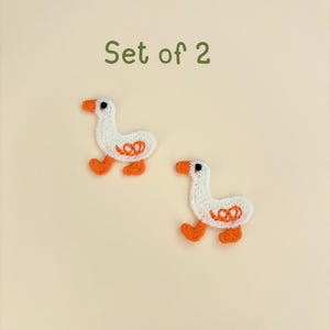 May include: Two white goose patches with orange beaks, feet, and decorative accents. The patches are embroidered and have a textured appearance. The text "Set of 2" is in green above the patches.