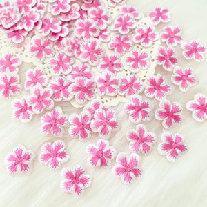 May include: A collection of pink and white embroidered flower appliques. The flowers have a white centre and pink edges.