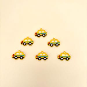 May include: Six embroidered yellow taxi cab patches with black wheels, a white roof, and a blue stripe. Each patch has red and green accents. The patches are arranged on a light beige background.