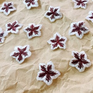 May include: A collection of white fabric flower appliques with maroon centers. The appliques are scattered on a brown paper background.