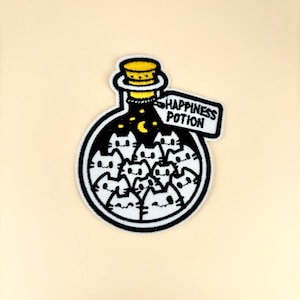 May include: Embroidered patch featuring a black and white illustration of a potion bottle filled with cat faces. The bottle has a yellow stopper and a tag that reads "HAPPINESS POTION". The patch is outlined in white.
