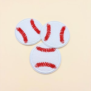 May include: Three circular white fabric patches, each featuring red embroidered stitching that mimics the appearance of baseball laces. The patches are arranged in a triangular formation, showcasing the detailed red thread texture against the white fabric.