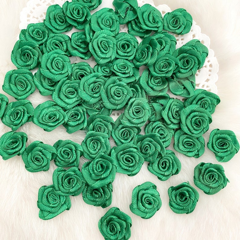 May include: A large collection of green fabric rosettes, arranged in a random pattern. The rosettes are made of a soft, silky fabric and have a delicate, ruffled texture.