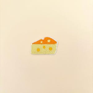 May include: An embroidered patch shaped like a wedge of Swiss cheese. The top section is orange with small yellow circles, while the bottom section is light yellow with larger yellow circles. The entire patch has a white stitched border edge.