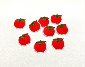 May include: A collection of nine embroidered patches shaped like red tomatoes with green stems. Each patch features dense red thread stitching for the fruit body and dark green thread for the stem detail, all arranged in a scattered pattern.