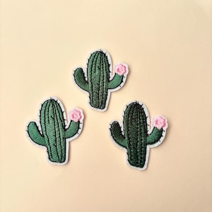 May include: Three embroidered cactus patches with pink flowers. The patches are green and white.