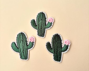 May include: Three embroidered cactus patches with pink flowers. The patches are green and white.
