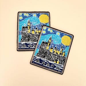 May include: Two rectangular embroidered patches featuring a stylized castle on a cliffside overlooking water. The design includes a swirling blue sky with yellow stars and a large yellow moon, rendered in vibrant thread colors with a black border.