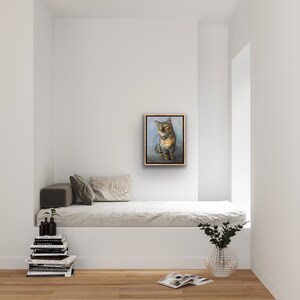 May include: A framed painting of a tabby cat sitting on a blue background. The cat has green eyes and a white patch on its chest.