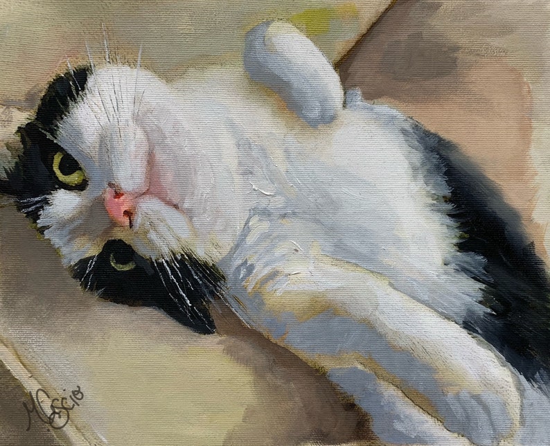 May include: A black and white cat with green eyes lies on its back on a beige surface. The cat's paws are in the air and its head is tilted back.
