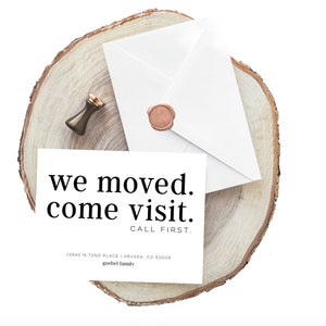 May include: A white card with the text "we moved. come visit. CALL FIRST." sits on a wooden slice, next to a white envelope sealed with a wax stamp. A bronze-colored wax seal and a small bronze stamp are also visible.