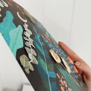 K&ouml;nnte beinhalten: Ein schwarzes Leinwandbild mit einem fantasievollen Blumendesign. Das Bild zeigt eine Vielzahl von Blumen, Bl&auml;ttern und anderen botanischen Elementen in Gr&uuml;n-, Blau-, Orange- und Wei&szlig;t&ouml;nen.