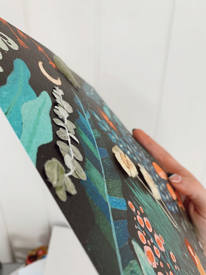 K&ouml;nnte beinhalten: Ein schwarzes Leinwandbild mit einem fantasievollen Blumendesign. Das Bild zeigt eine Vielzahl von Blumen, Bl&auml;ttern und anderen botanischen Elementen in Gr&uuml;n-, Blau-, Orange- und Wei&szlig;t&ouml;nen.