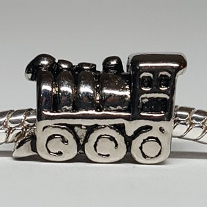 May include: Silver charm in the shape of a train engine. The charm has a detailed design with wheels and a smokestack.