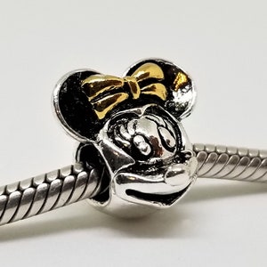 May include: Silver charm featuring a black and white image of Minnie Mouse with a gold bow.