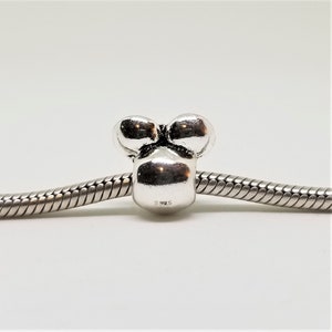 May include: Silver charm bead with three round bumps, resembling a stylised flower or a cluster of grapes. The bead is marked with "S925" on the bottom.