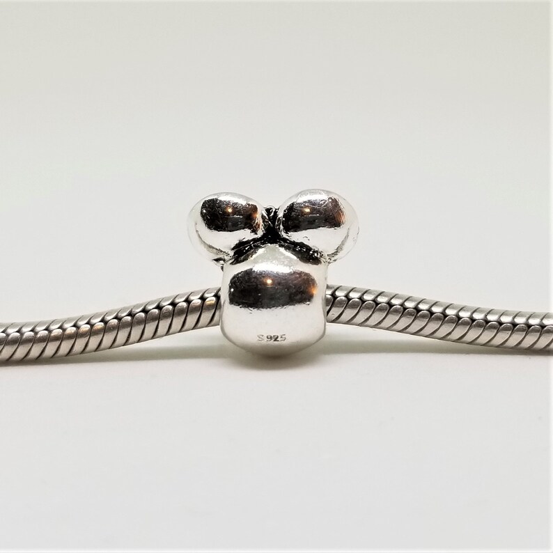 May include: Silver charm bead with three round bumps, resembling a stylised flower or a cluster of grapes. The bead is marked with "S925" on the bottom.