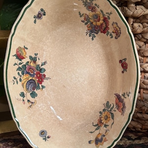 May include: A beige, scalloped-edge serving platter with a green border. The platter is decorated with floral bouquets in shades of red, yellow, blue, and purple. The overall design is reminiscent of vintage tableware.