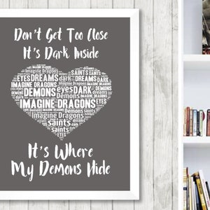 May include: A gray and white printable wall art design with a heart-shaped word cloud. The text in the word cloud includes "Imagine Dragons", "Demons", "Saints", and "Dreams". The text below the word cloud reads "Don't Get Too Close It's Dark Inside It's Where My Demons Hide".