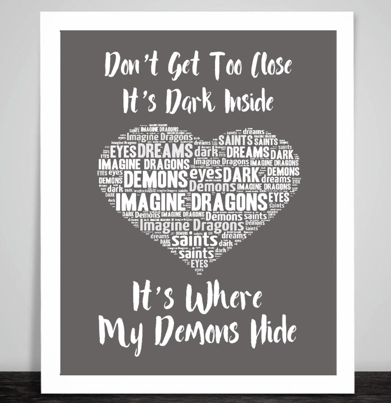 May include: A gray background with white text that reads "Don't Get Too Close It's Dark Inside" and a heart-shaped word cloud with the words "Imagine Dragons" and "Demons" repeated many times. The text below the heart reads "It's Where My Demons Hide".