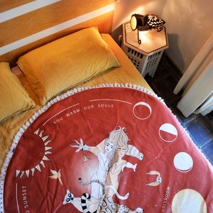 May include: Circular, terracotta-coloured beach towel with a white fringe. The towel features a celestial design with two figures, sun, moon phases, and the text "YOU WARM OUR SOULS" and "SUN FROM SUNRISE TO SUNSET".