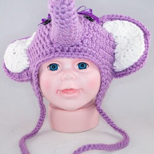 May include: Purple crocheted elephant hat with white ears and a long purple tie. The hat is on a doll's head.