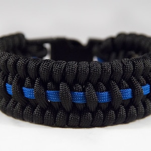 May include: Black paracord bracelet with a single blue stripe woven into the design. The bracelet is a symbol of support for law enforcement.