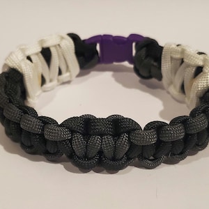 May include: A black, white, and purple paracord bracelet with a sliding knot closure.