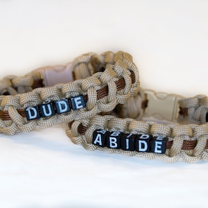 May include: Two brown and tan paracord bracelets with black letter beads spelling out "DUDE" and "ABIDE".
