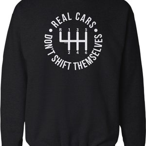 May include: Black sweatshirt with a white graphic of a stick shift gear pattern and the text "Real Cars Don't Shift Themselves".